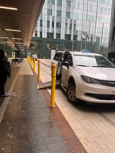 Taxi adapté avec sa rampe abaissée, en attente d’un passager en fauteuil roulant devant le CHUM à Montréal.